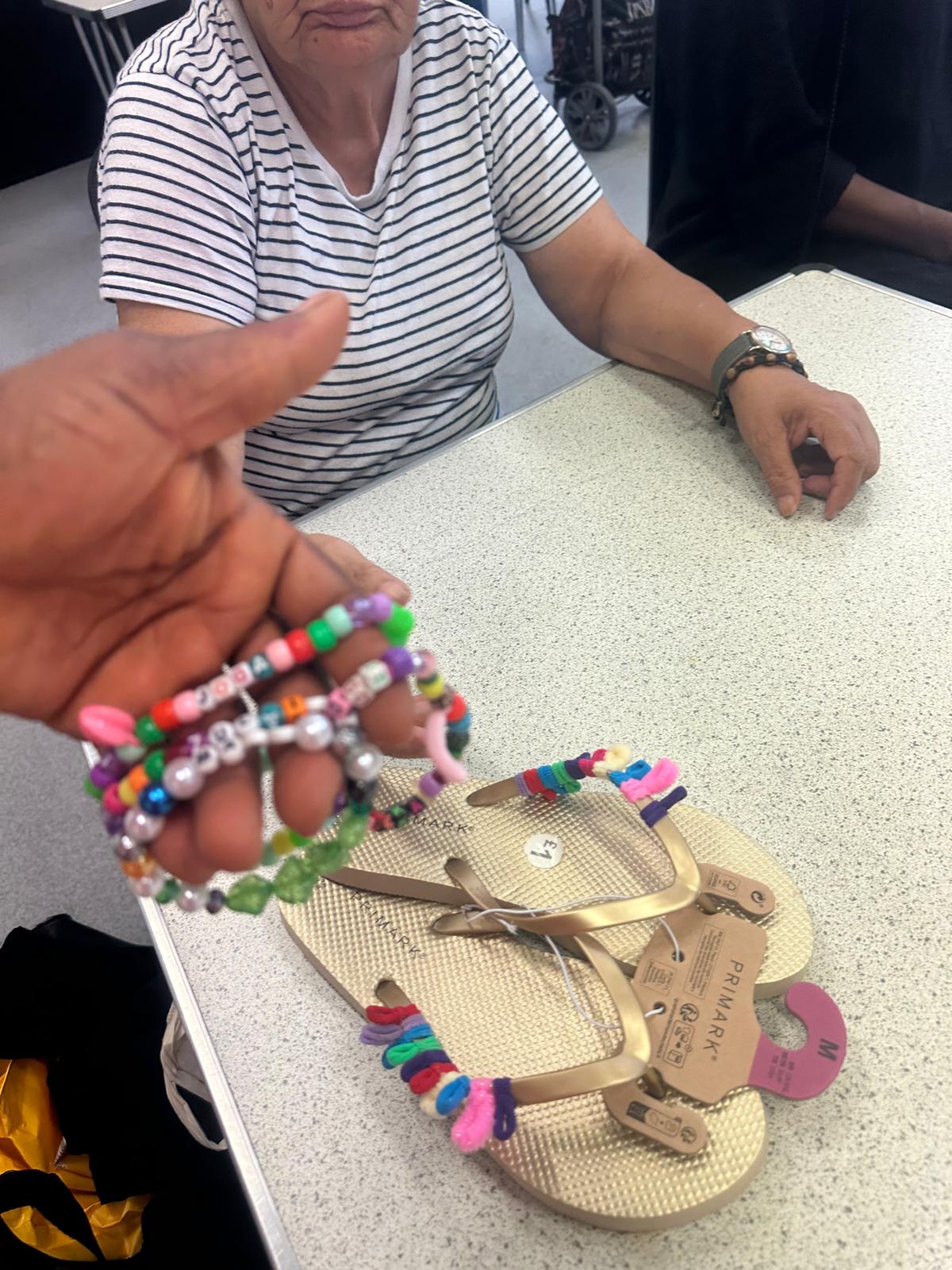 Hands showing off multiple colorful beaded bracelets and decorated flip-flops as finished craft projects