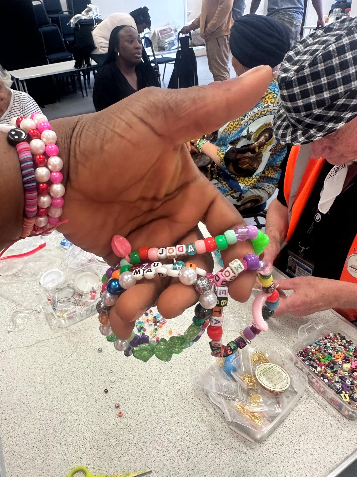 Hands displaying beautiful finished beaded bracelets with letter beads spelling names and words