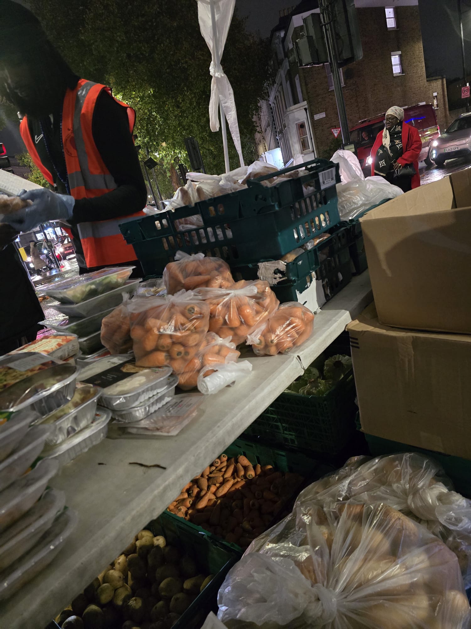 Street outreach setup with fresh produce, bread rolls, and prepared meals on outdoor tables at night